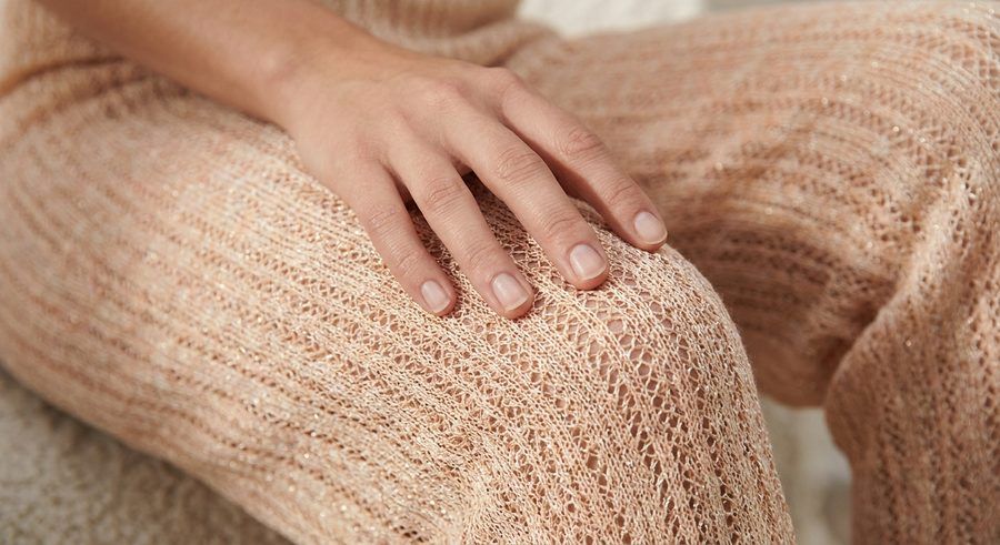 Detalle de un pantalón de punto calado color melocotón con hilo metálico